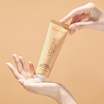 Woman’s hands holding Vegan Body Crème Tangerine Glow on an orange background.