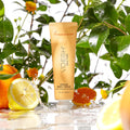 Vegan Body Crème Tangerine Glow in front of orange flowers, green leaves, lemon, and orange slices.