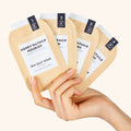 hand holding all 4 steps of Honey Oatmilk Nourish Pedi in a Box Deluxe 4 Step