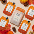 Pumpkin Pie Pedi In a Box with Packets surrounded by pine cones, autumn leaves, and pumpkins on beige background