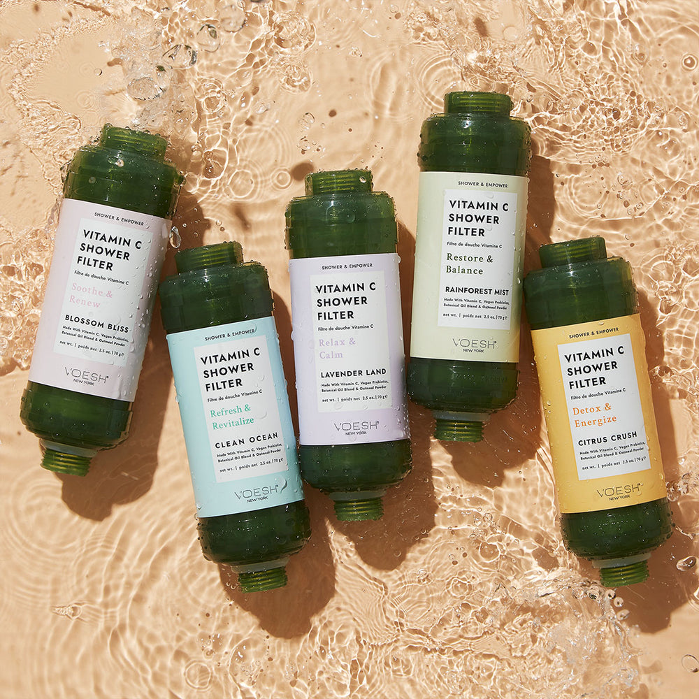 Five Vitamin C Shower Filters in each scent lined up on a tan water background.