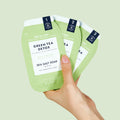 Woman's hand holding green tea detox 3 step packets on green background
