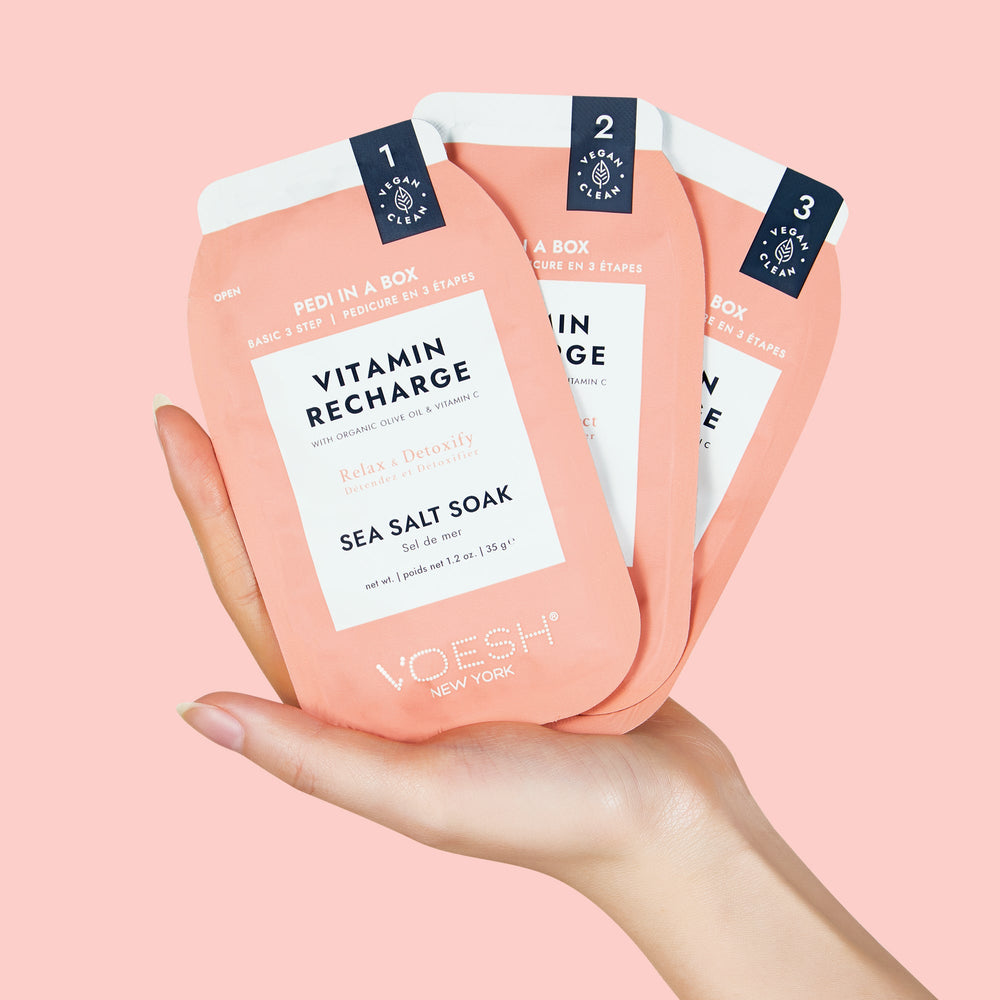 woman's hand holding vitamin recharge pedi in a box 3 step on light pink background