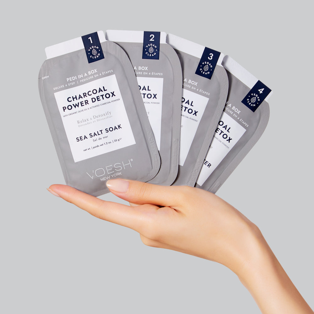 Woman's hand holding packets of pedi in a box 4 step charcoal detox
