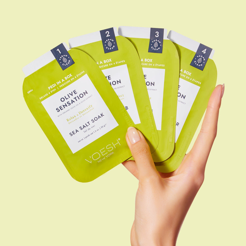 woman's hand holding pedi in a box 4 step olive sensation packets on green background