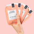 woman's hand holding vitamin recharge pedi in a box 4 step packets on pink background