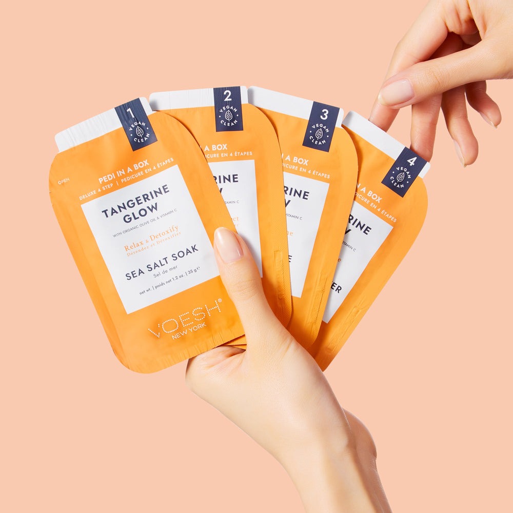 woman's hand holding tangerine glow pedi in a box 4 step packets on orange background