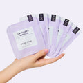 Woman's hand holding Lavender Vanilla O2 fizz packets on light purple background
