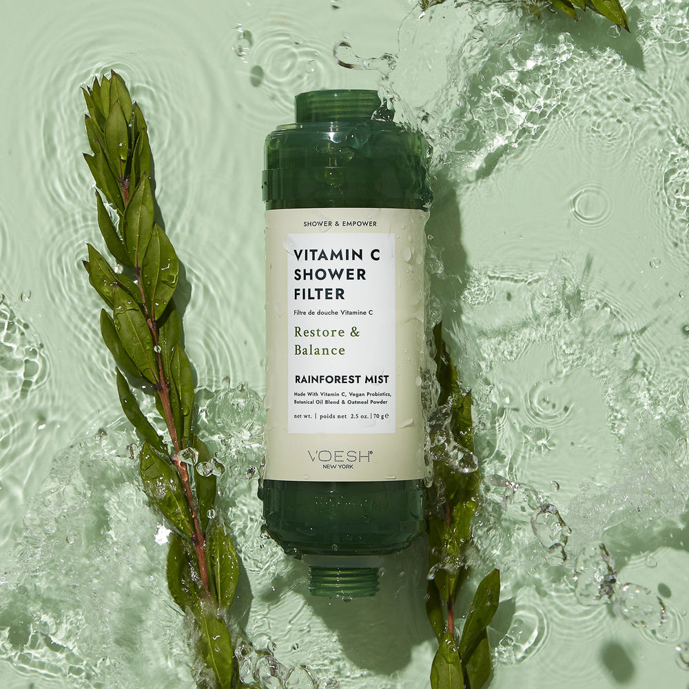 Rainforest Mist Vitamin C Shower Filter in water with green leaves surrounding it on green background