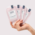 Woman’s hand holding 4 sachets from Pedi Moments Jasmine Soothe on a pink background.