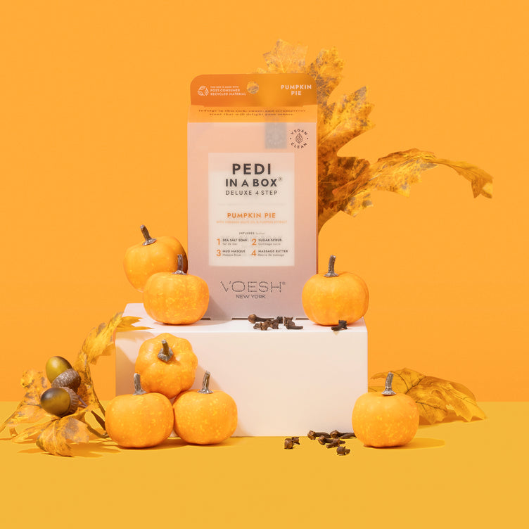 Pumpkin Pie Pedi In a Box with Packets surrounded by pine cones, autumn leaves, and pumpkins on orange background