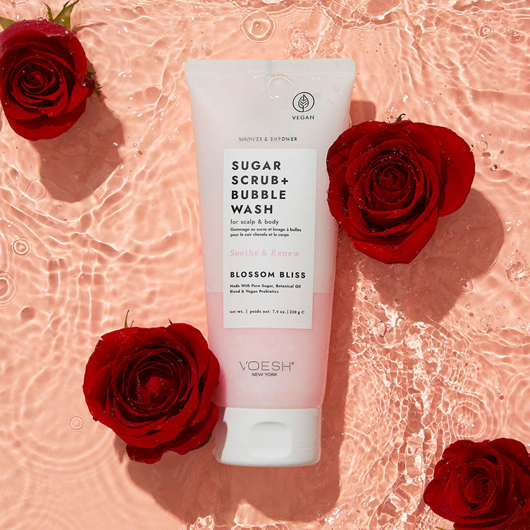 Sugar Scrub + Bubble Wash Blossom Bliss next to roses on a pink water background.