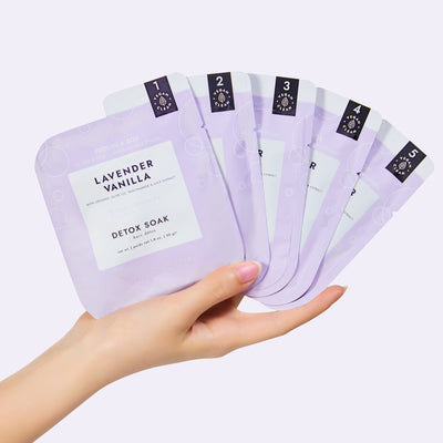 Woman's hand holding Lavender Vanilla O2 fizz packets on light purple background