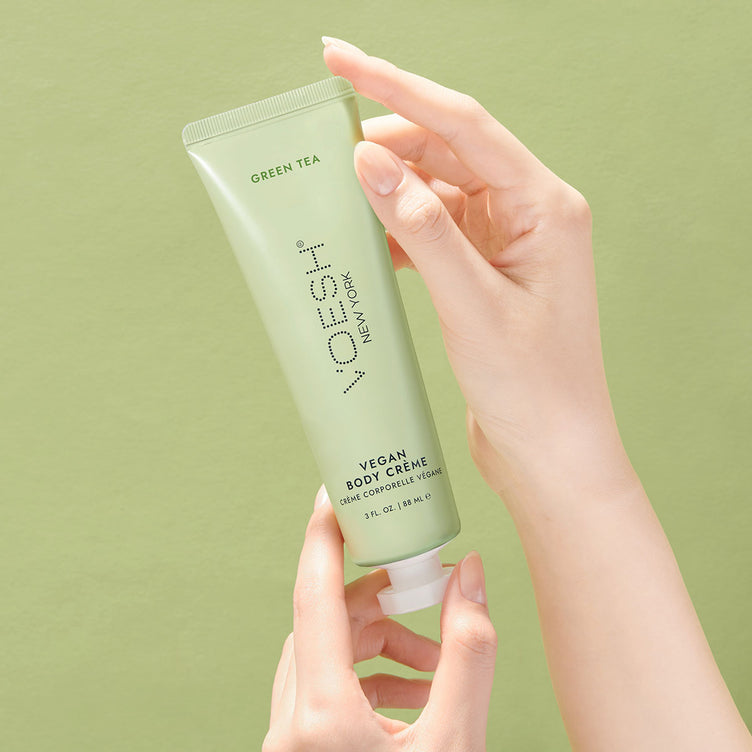 Female hands holding VOESH’s Green Tea Vegan Body Crème, in front of a green background, for healthy, hydrated skin.