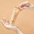 Female hands holding VOESH’s Tangerine Glow Vegan Body Crème, in front of an orange background, for healthy, hydrated skin.