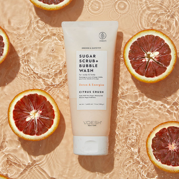 Citrus Crush Shower & Empower Sugar Scrub in water with citrus fruits on orange background