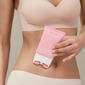 Woman in her bra and underwear holding Smooth’d Body Refining Roller Crème in front of her stomach pictured on a tan background.